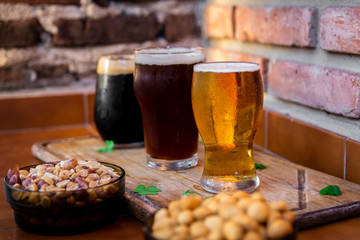 tres tipos de cerveza rubia, roja y negra, sobre una tabla de madera, con mani, fondo de ladrillos