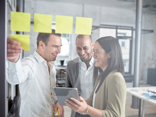 Happy colleague with sticky notes and tablet in office