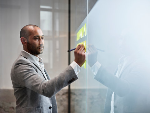 Businessman writing on sticky notes at glass pane in office