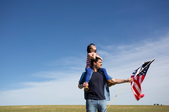 Man with daughter and American flag on field in remote landscape - Powered by Adobe
