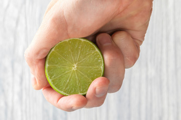 The hand of a man squeezes the juice from a slice of lime half. Juicy drop hanging down.