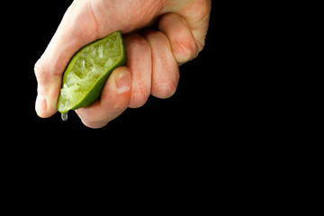 The hand of a man squeezes juice from half a lime. Juicy drop hanging down.
