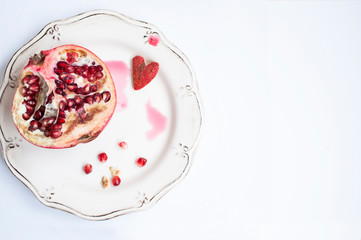 half juicy pomegranate with little heart on plate. Space for text