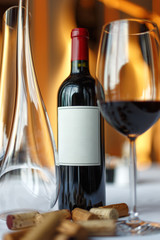 bottle of red wine, a glass of wine and a decanter on a table with a white tablecloth.