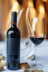 bottle of red wine, a glass of wine and a decanter on a table with a white tablecloth.