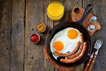 Fried eggs and thin sausages in a cast iron skillet. Breakfast. Top view.