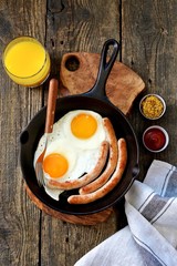Fried eggs and thin sausages in a cast iron skillet. Breakfast. Top view.