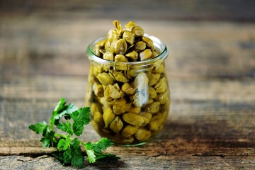 Marinated capers in a glass jar on a wooden background.
