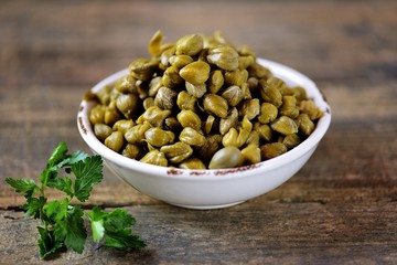 Marinated capers in a glass jar on a wooden background.