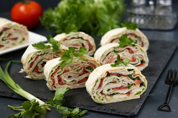 Lavash roll with smoked chicken, tomatoes, cheese and greens located on a dark background