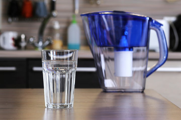 Glass of clean water and filter for cleaning drinking water on the table in the kitchen. Purification of drinking water at home.