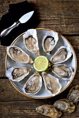 Fresh ocean oysters with slices of lemon on ice on old wooden background. Top view. 
