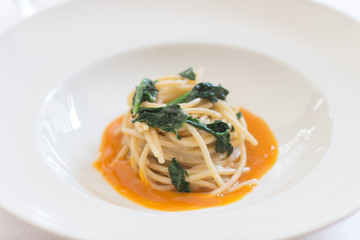 Close up on a white dish with italian food pasta an orange juice and vegetables.