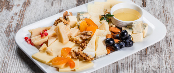 Cheese platter garnished with pear, honey, walnuts in plate over rustic background. Snacks and Wine appetizers set