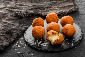 Fried potato cheese balls or croquettes with spices on black plate over dark stone background....