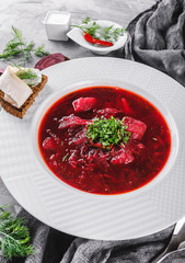 Ukrainian and Russian traditional beetroot soup - borscht in plate with spice, garlic, greens on rustic background, healthy food. Ingredients on table. Top view, flat lay