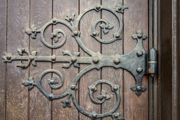 close up of big ornate cast iron door hinge on wood plank door