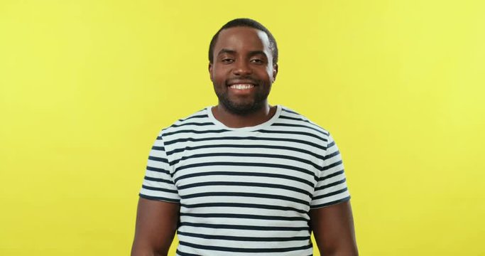 Portrait of the young African American happy handsome guy in striped T-shirt standing on the yellow backgroung and smiling to the camera.