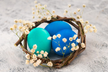 Fototapeta na wymiar Painted chicken eggs in a nest for Easter. White spring flowers on a light background.
