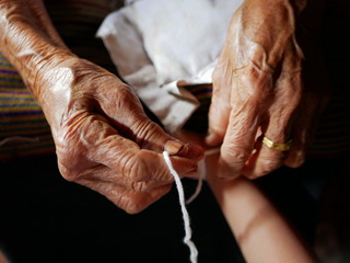 Hand of old woman waving a white string ( Sai Sin ) around her granddaughter hands - Thai traditional blessing from an elder one