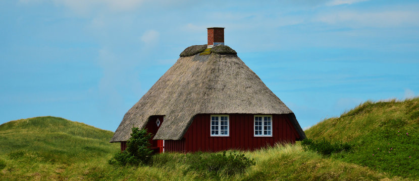 Haus in den D&uuml;nen mit Reetdach unter blauem Himmel