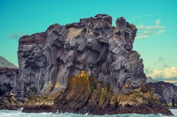 Jagged rock formations coming out of the ocean off of the Westman Island coast in Iceland with blue sky