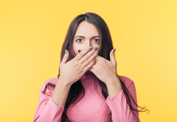 Surprised excited woman covering her mouth with hands on yellow background