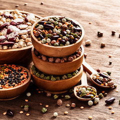 Mixed raw dried Indian legumes in wooden bowls on rustic background.