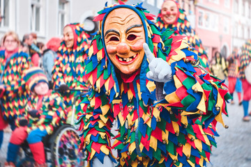 Colorful carnival figure with pretty wooden mask shows a gesture with the index finger. Street...