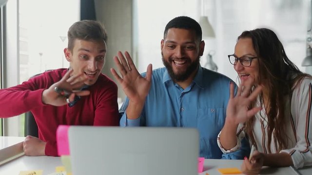 Smiling young people having conversation through laptop. Cheerful business consultants smiling and waving to camera. Business and technology concept