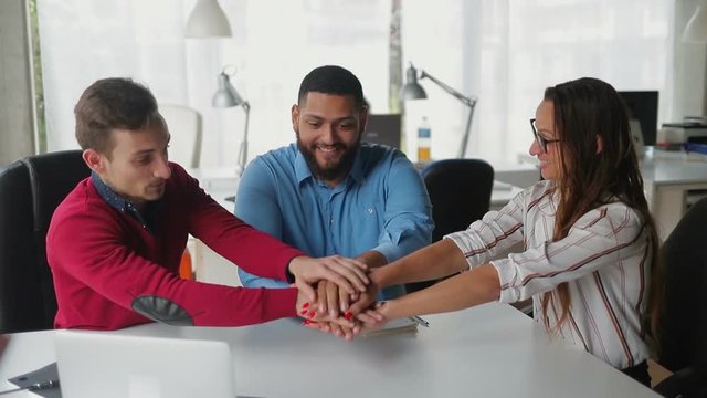 Smiling employees putting hands together. Successful business team sitting at table in modern office. Concept of team building