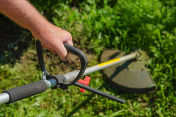 Man farmer mows the grass trimmer. Portrait of a close-up hand mowing grass. Cut the lawn.