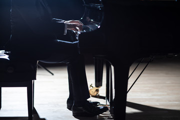An elegant man in a black suit playing grand piano on stage in a concert hall, close up,...