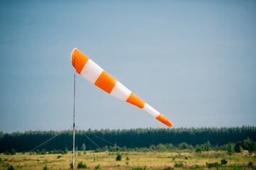 Red and white windsock blows against a blue sky on green glade