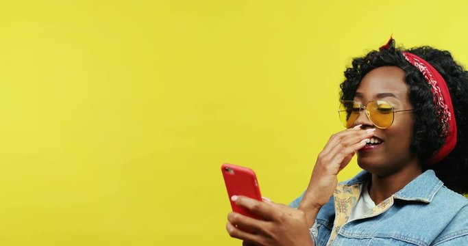 Close up of the beautiful young African American woman texting a message on the smartphone while chatting in social medif. Yellow background.