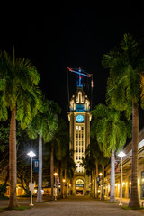 Aloha Tower lit up at night with a path lined with palm trees