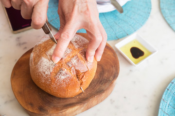 Hands cutting baguette bread loaf on wooden board