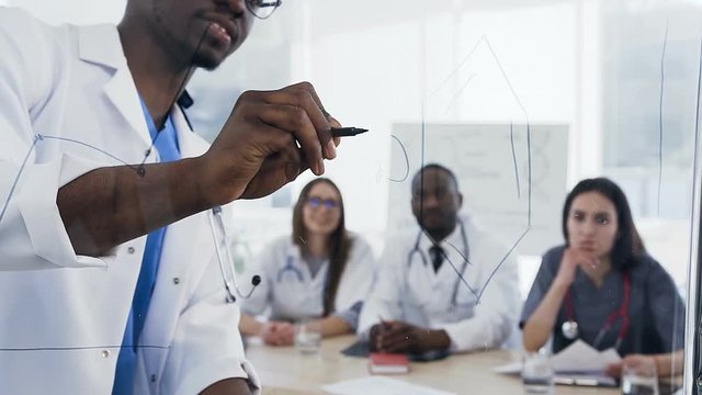 Close up shot of male doctor writting on the board during lection in the young intern in the conference room.