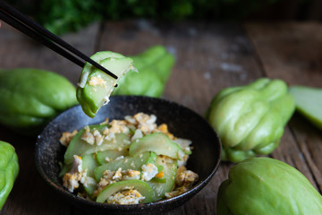 Fresh chayote fruits (Sechium edulis) stir fried with egg and garlic in bowl on wood background