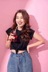 portrait of beautiful happy cute woman girl in casual summer clothes drink red soda water from bottle with straw over pink background