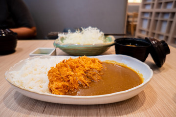Selective focus of deep fried crispy cutlet pork with japanese style yellow curry and rice in white ceramic dish eating together with soy miso soup and cabbage salad.