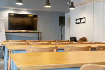 Small empty classroom or meeting room interior with modern wooden table, chairs and lamps. Learning media with television, audio and whiteboard.