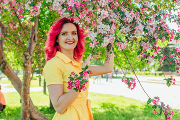 Beautiful and young woman with bright red hair and ref lips standing next to a blooming apple tree...