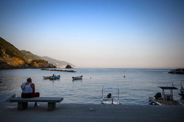 Liguria / Italy - June 24 / 2016 : A middle aged man sitting on a coach at coast and looking to sea with boats