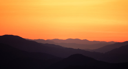 Landscape view black mountains and forest silhouette under skyscape orange gradients morning sunlight with mist and fog. Northern in Thailand.