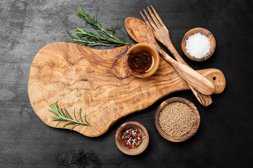 Cutting Board, rosemary and spices on a black wooden table.