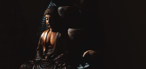 Golden Gautama Buddha statue with a black background depicting darkness and hope coming in form of...