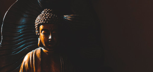 Golden Gautama Buddha statue with a black background depicting darkness and hope coming in form of sunlight. - obrazy, fototapety, plakaty