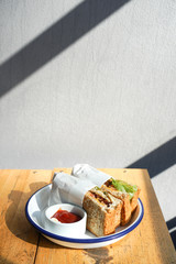Sandwiches in white plate with ketchup and mayonnaise on a wooden table.