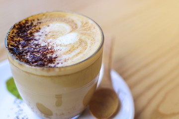 Hot latte juice in a glass with a white coaster with a wooden spoon placed on a beautiful wood table.